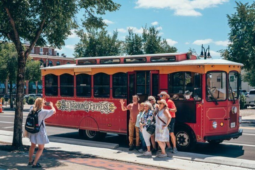 A red vintage bus with 'Old Fashioned Express' written on the side, parked on a street with people standing around it. 1
