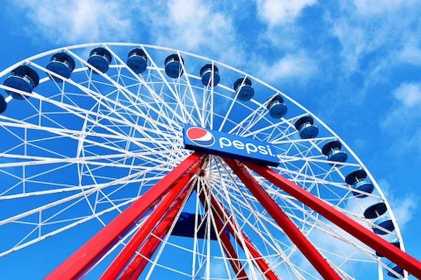 A large Ferris wheel with red and white structures and a Pepsi logo at the center against a blue sky. 2