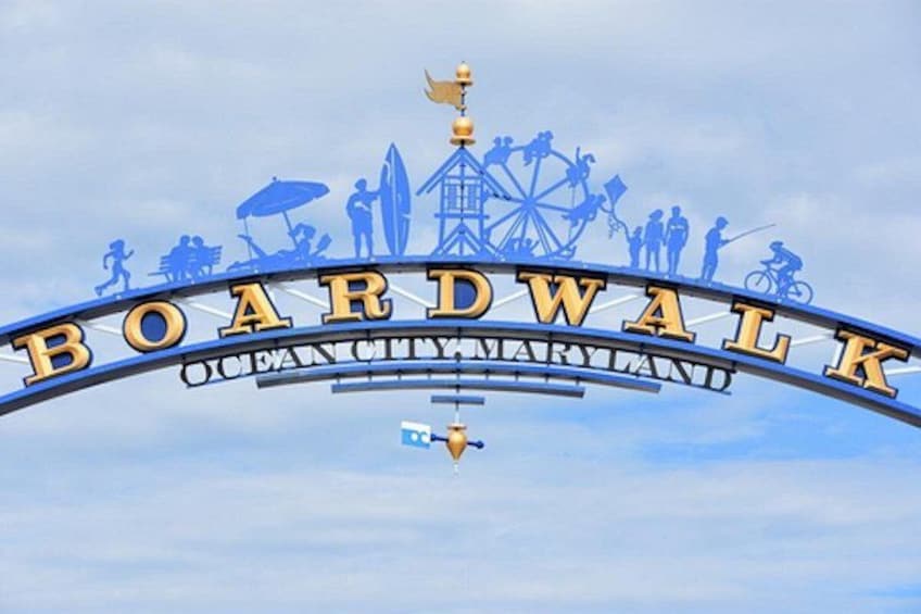 A sign with the text 'Boardwalk Ocean City Maryland' and silhouettes of various activities like walking, cycling, and a Ferris wheel. 1