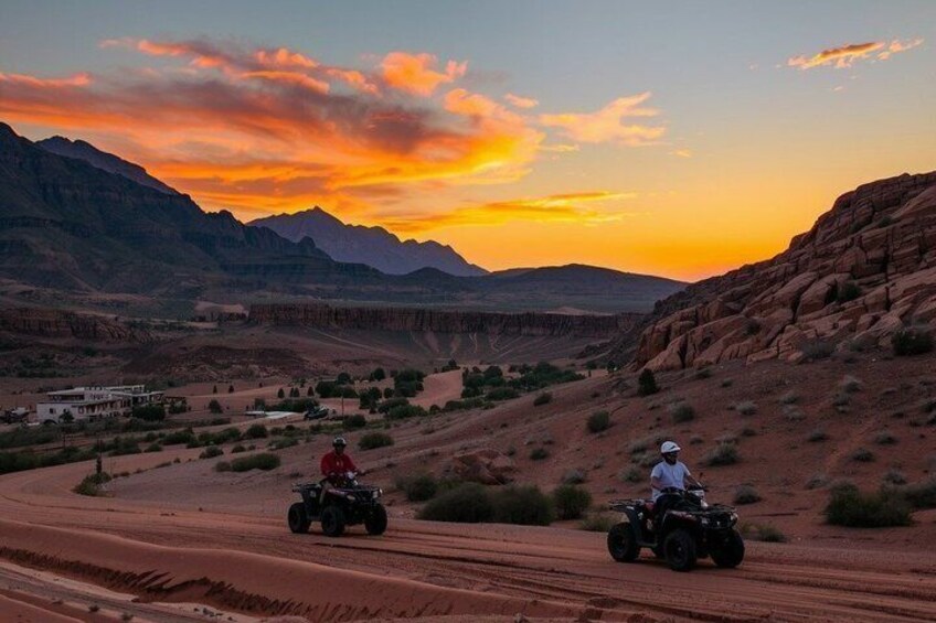 Dos personas conducen cuatrimotos por un camino de tierra, con una puesta de sol y montañas al fondo. 4