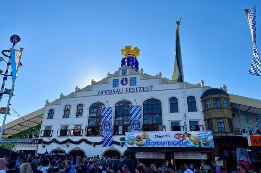 A historic building with a sign reading 'HOFBRÄU FESTZELT' and a large blue and white checkered flag. 2