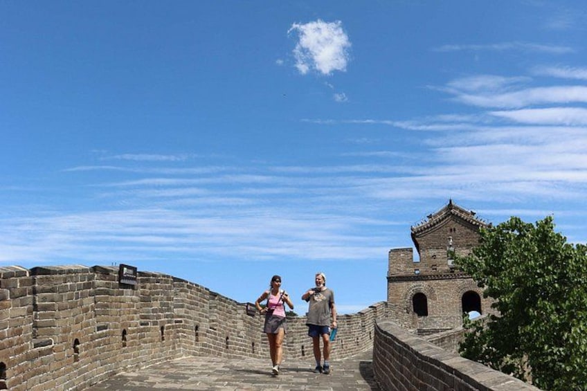 Two people walking along the Great Wall of China, with clear blue skies and a brick structure in the background. 2