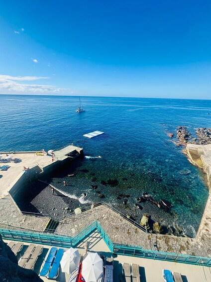 A coastal scene with clear blue waters, a rocky shoreline, and a pier with lounge chairs. 2