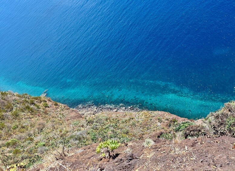 A coastal landscape with clear blue waters, rocky terrain, and sparse vegetation. 4
