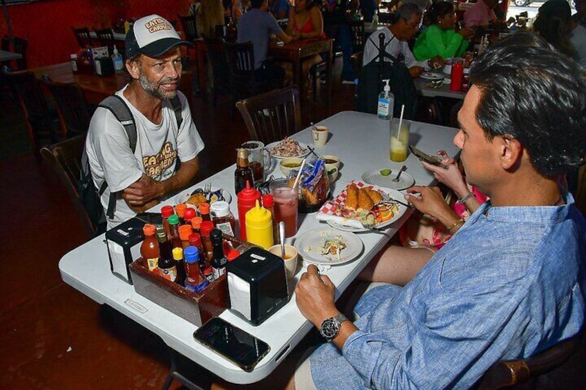 Dos personas cenando en un restaurante, con varios condimentos y un teléfono inteligente sobre la mesa. 5