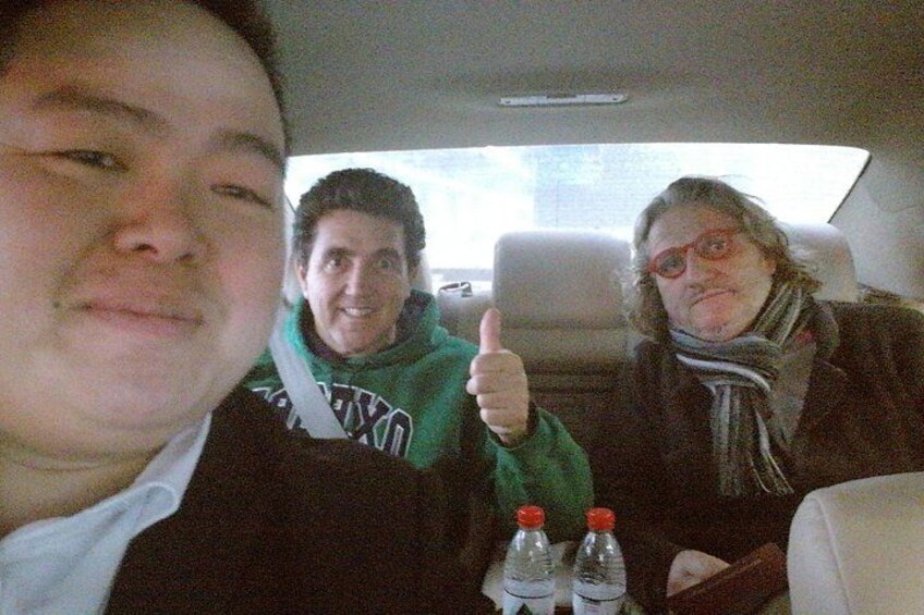 Two people in a car, one giving a thumbs up, with a bottle of water on the seat. 1