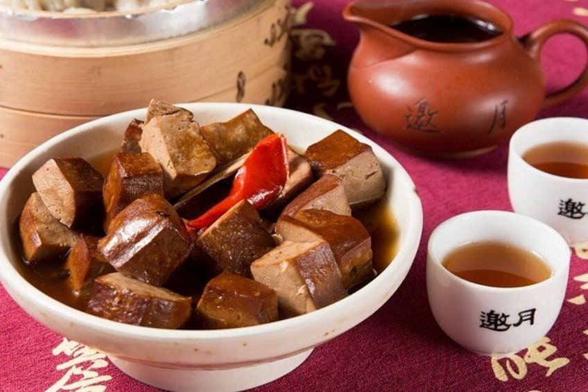 Un tazón de carne cocida con un chile rojo, una olla de barro y dos tazas de té sobre una mesa. 2