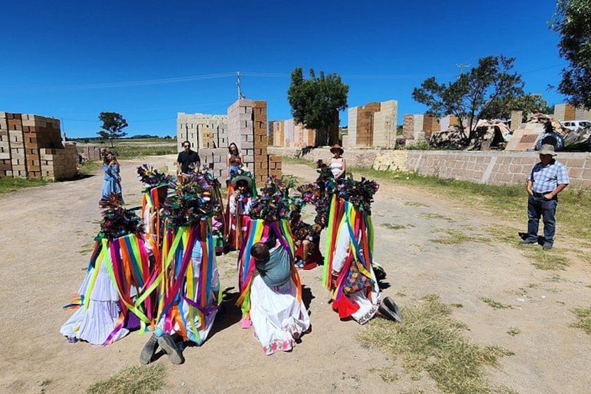A group of people with colorful decorations, possibly for a cultural event, in a rural setting with buildings and a clear sky. 3