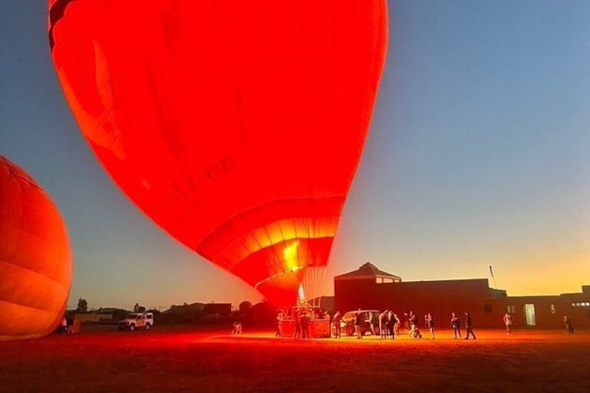 En varmluftsballon med besætning der forbereder sig til start, en klar himmel og en bygning i baggrunden. 3