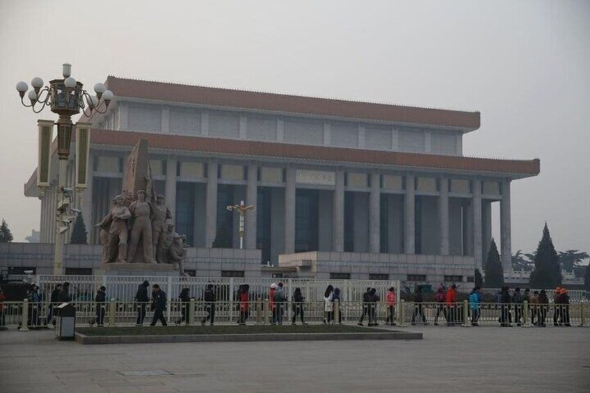 A large building with a red roof and columns, surrounded by a fence with people walking around. 2