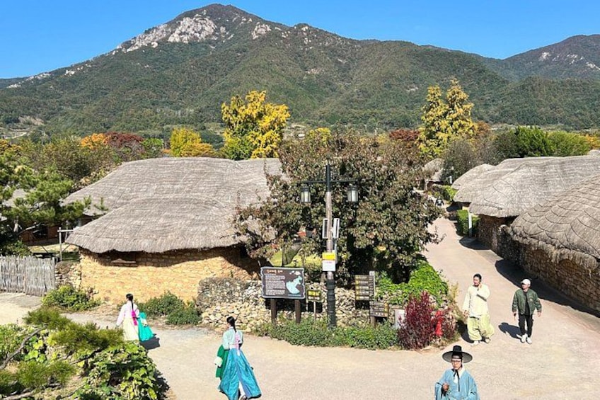 A rural village with traditional thatched-roof houses, a clear sky, and mountains in the background. 4