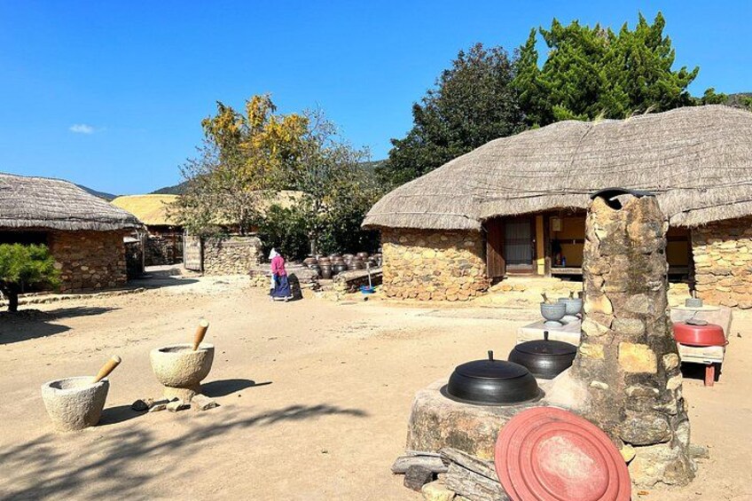A rural village with thatched-roof houses, a woman in traditional attire, and traditional cooking utensils. 5