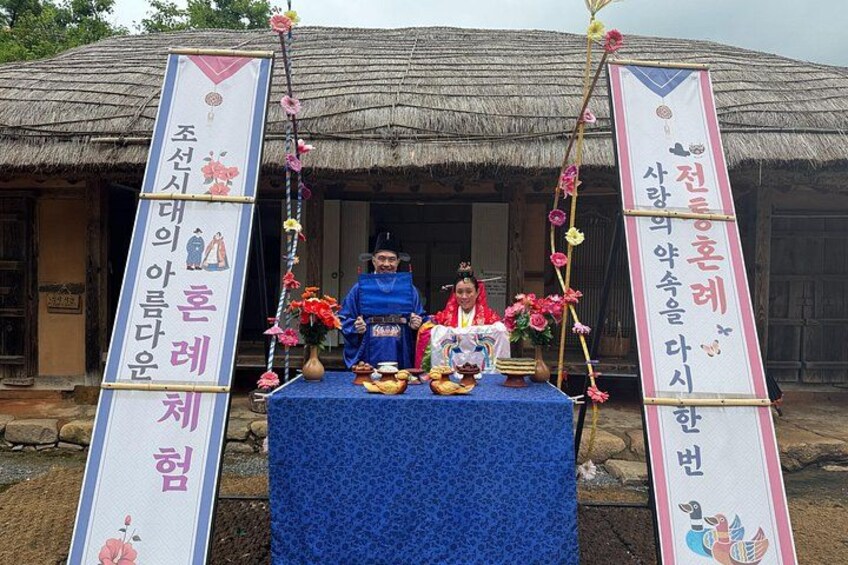 A traditional Korean shrine with a blue tablecloth, two figures in traditional attire, and a signboard with Korean text. 5