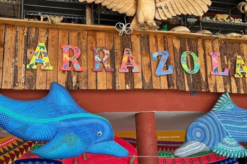 Un cartello di legno con lettere colorate che formano la scritta 'ARRAZOLA' e sculture decorative a forma di pesce sottostanti. 2