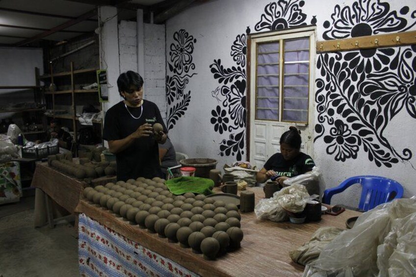 A workshop with decorative wall art, a person working with clay pots, and another person seated. 4
