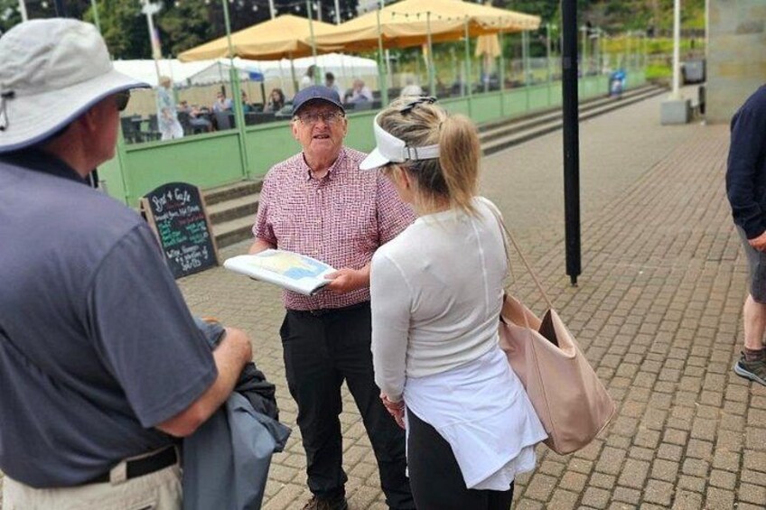 A group of people standing outdoors, possibly at a market or outdoor event, with a chalkboard sign in the background. 5