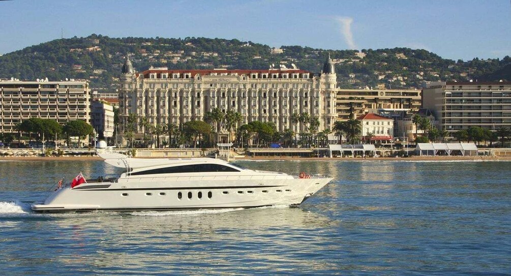 A white yacht on calm water with a large building and trees in the background. 1