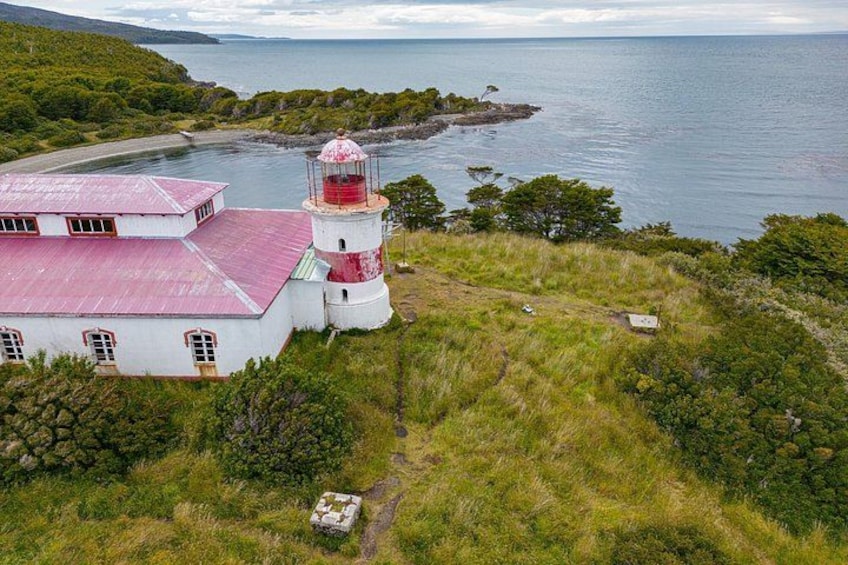 Un phare avec un sommet rouge, un bâtiment blanc avec un toit rouge et un paysage verdoyant avec un sentier menant au phare. 2