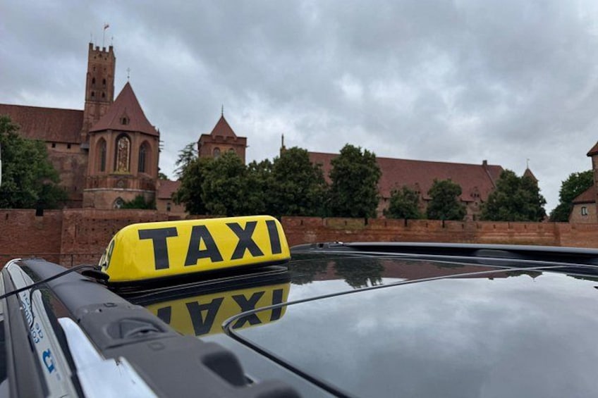 Un coche con la señal de taxi amarilla, un edificio parecido a un castillo y un cielo nublado. 3