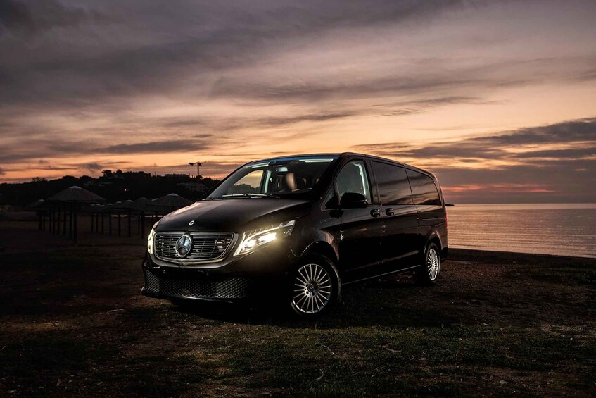 A black minivan parked on a grassy area near a body of water during sunset. 4