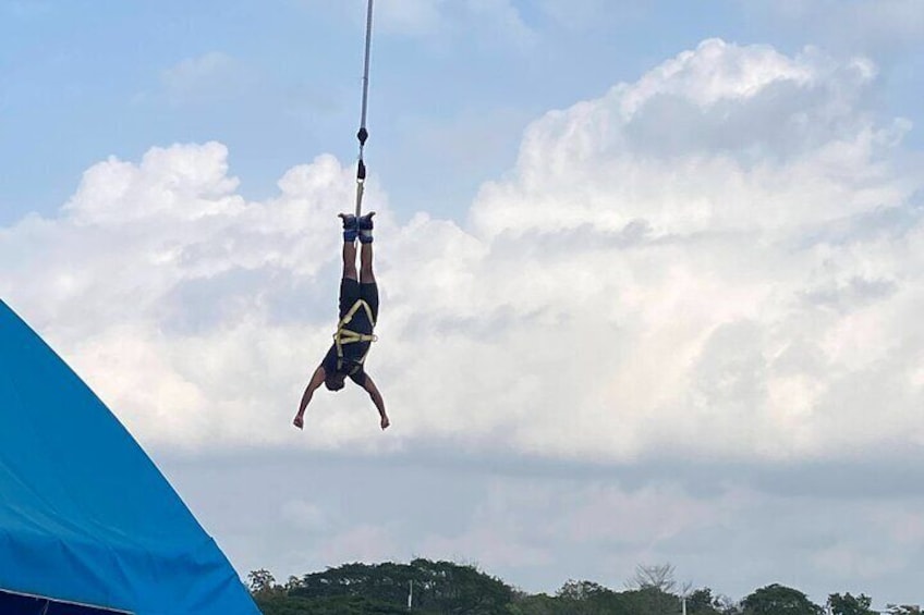 Una persona realizando una acrobacia aérea, sujeta por una cuerda, con un fondo de nubes y árboles. 1