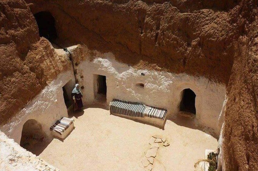 A narrow canyon with a person standing near a doorway, a bench, and a small structure. 1