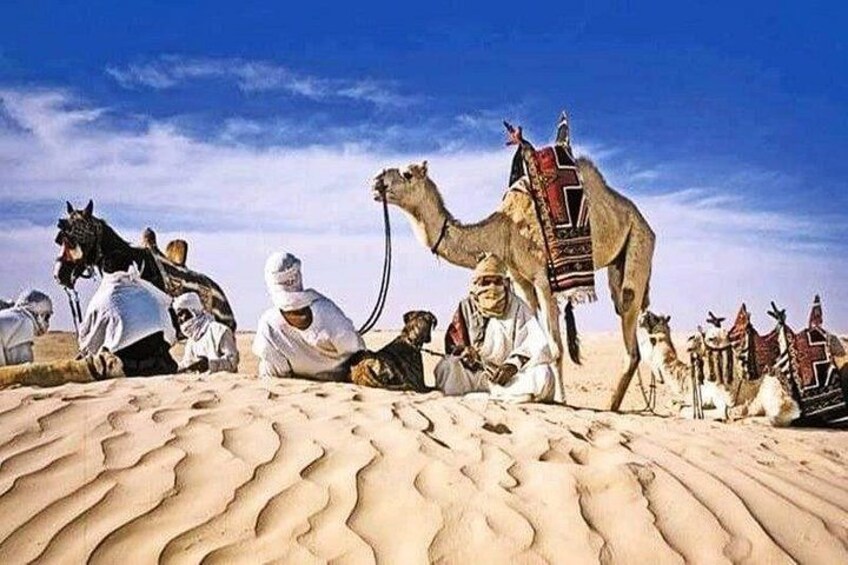 A camel caravan in a desert with people sitting on the sand. 2