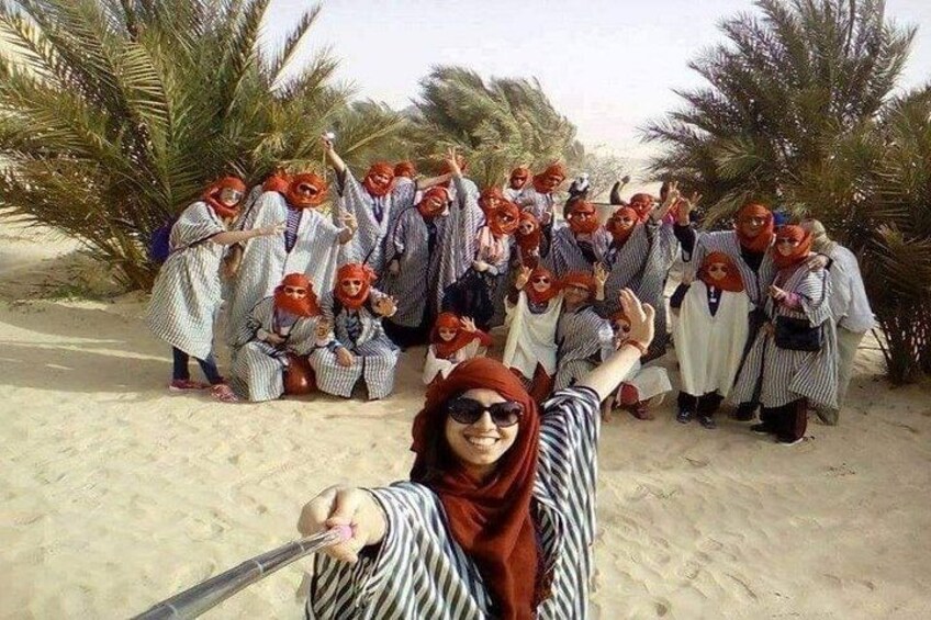 A group of people in traditional attire posing on a sandy beach with palm trees in the background. 5