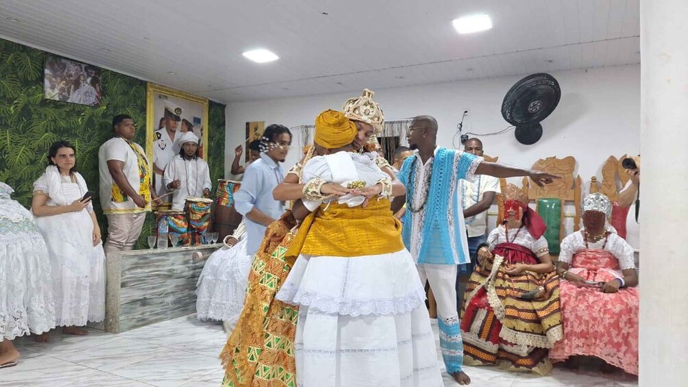 Una ceremonia tradicional con participantes vestidos con atuendos coloridos, una audiencia sentada y un interior decorado. 4