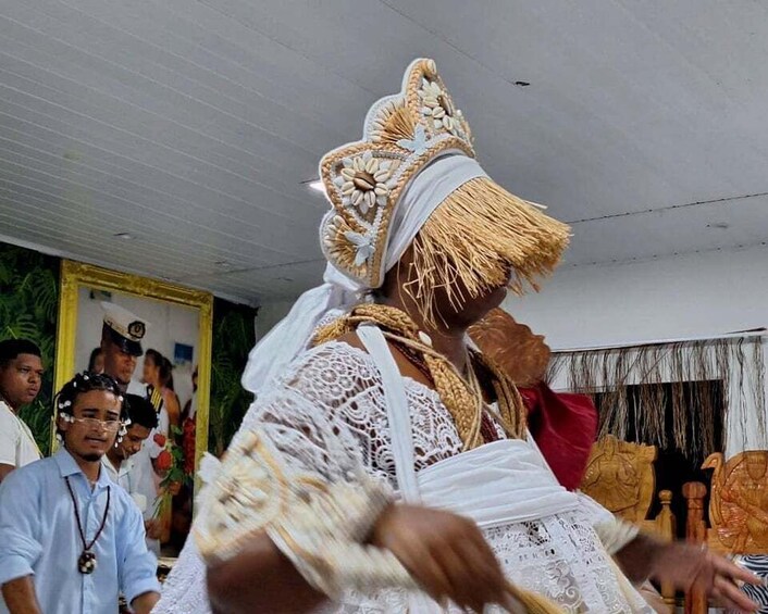 Una persona vestida con traje tradicional, sombrero de paja y prenda de encaje blanco, actuando frente a un público. 2