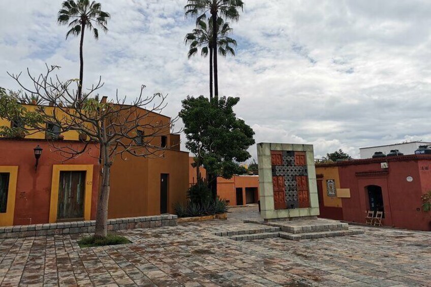 A courtyard with tiled flooring, palm trees, and buildings with yellow and red walls. 5