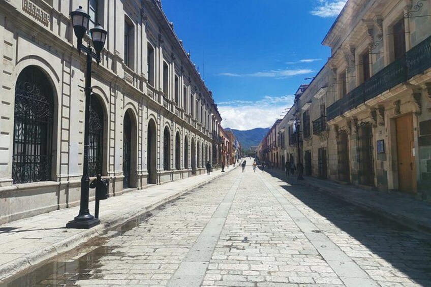 A cobblestone street lined with historic buildings, a clear sky, and a distant mountain range. 2