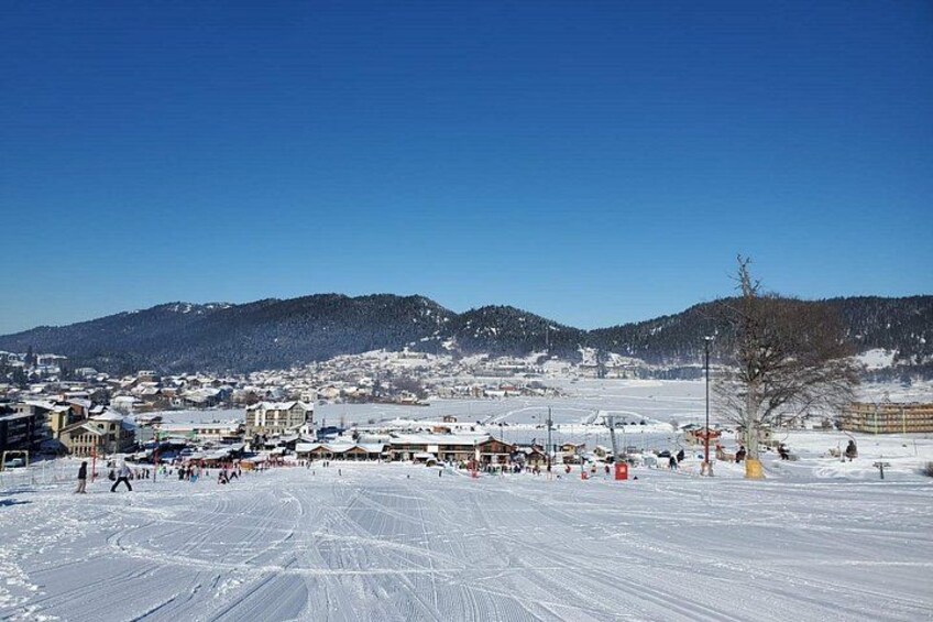 A snowy landscape with a town in the background, a clear blue sky, and a few people on the snow. 2