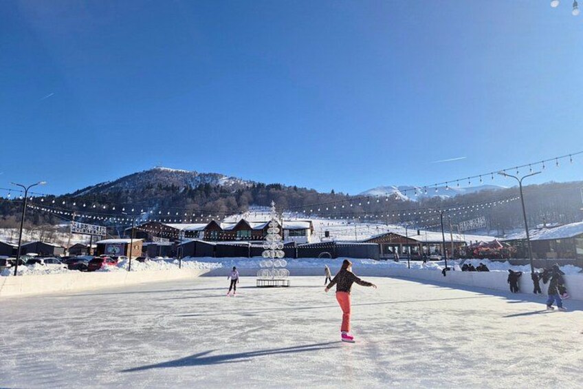 A snowy landscape with a person in pink pants and a black jacket, a ski lift, and buildings in the background. 4
