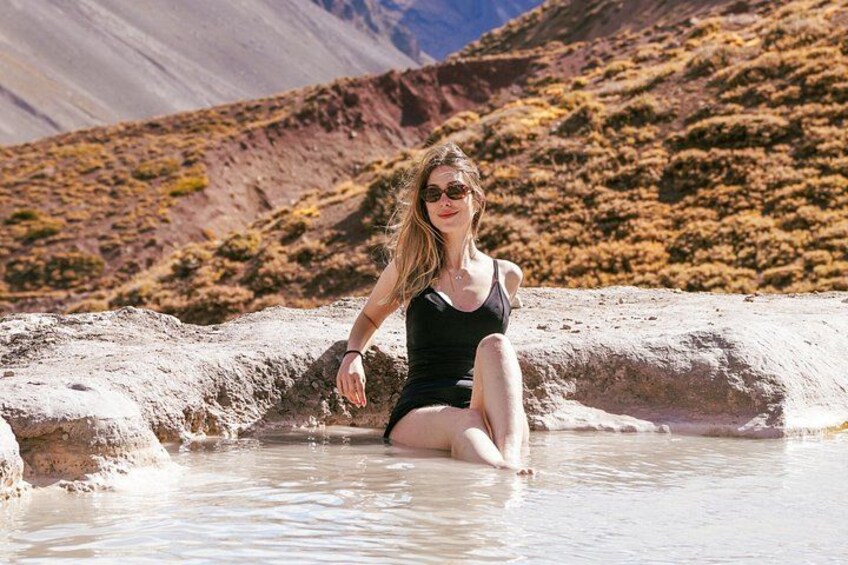 Una persona sentada en una piscina natural rodeada de terreno rocoso y montañas. 1