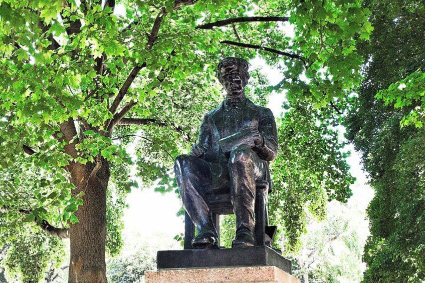 Eine bronzene Statue eines sitzenden Mannes mit einem Buch, umgeben von Bäumen. 3