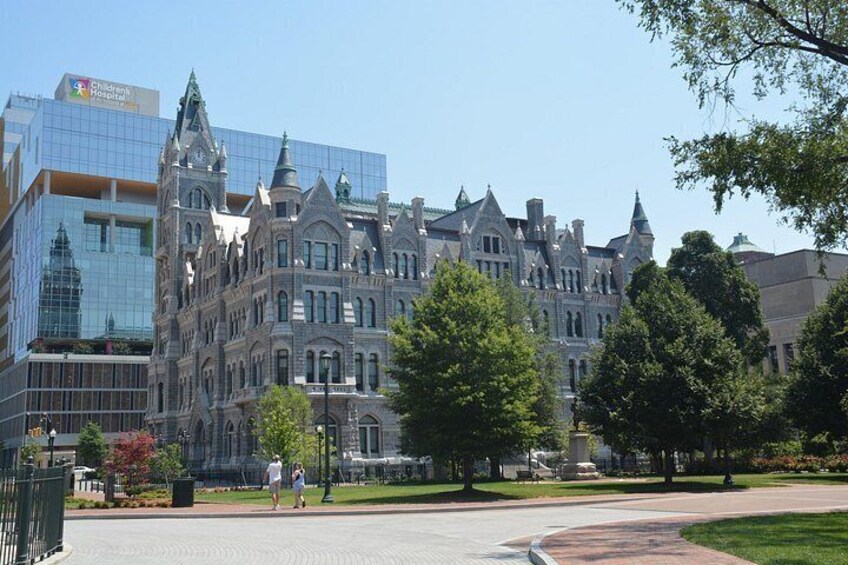 A historic building with ornate architecture, a modern glass building adjacent to it, and a well-maintained grassy area with trees. 2