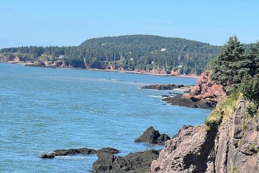 A coastal landscape with clear blue water, rocky cliffs, and a forested hill in the background. 1