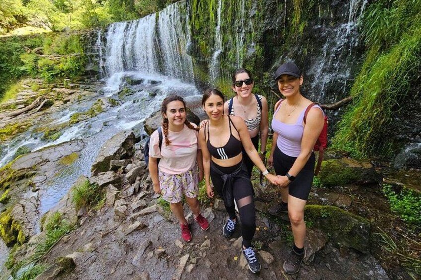 A group of people standing on a rocky path with a waterfall in the background. 1