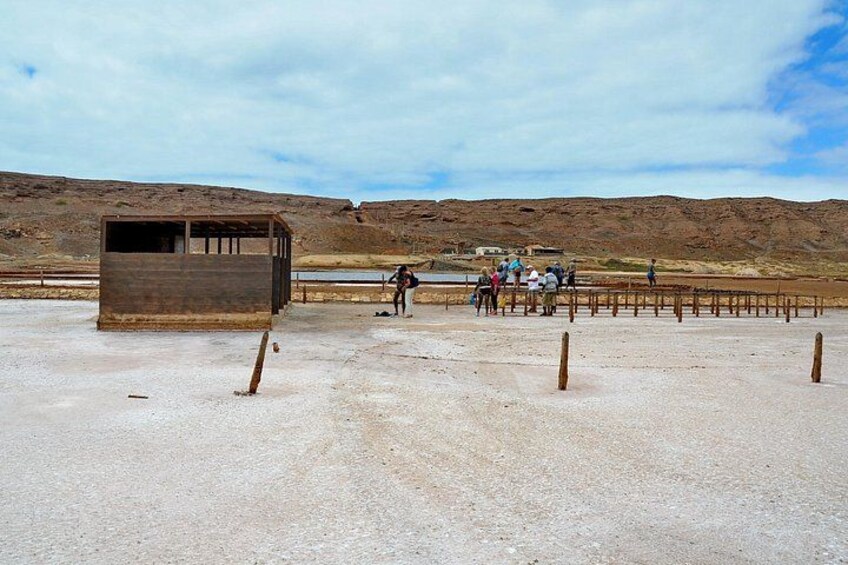 A barren landscape with a small wooden structure, a group of people gathered near a fence, and a distant hill. 2