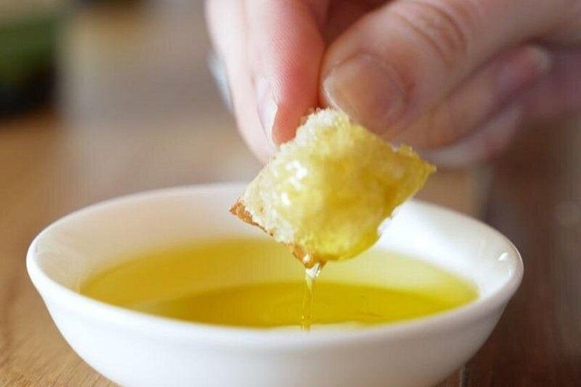 A hand dipping a piece of bread into a bowl of oil. 2