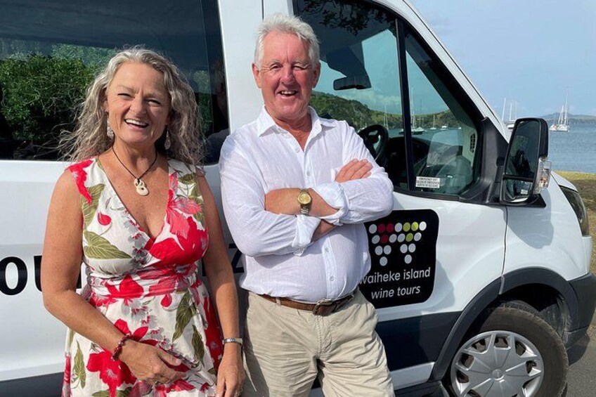 Two people standing in front of a white van with a logo and text indicating wine tours on Waiheke Island. 3