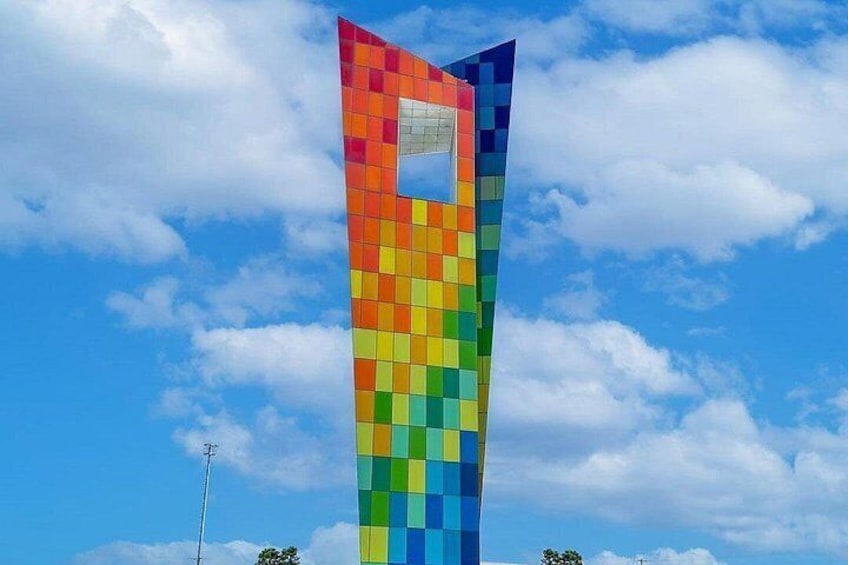 A tall, colorful, pixelated structure against a blue sky with clouds. 3