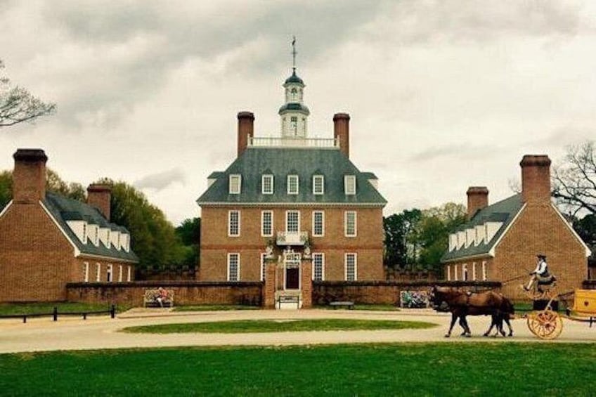 A historic brick building with a central tower, surrounded by a well-maintained lawn and a horse-drawn carriage. 2