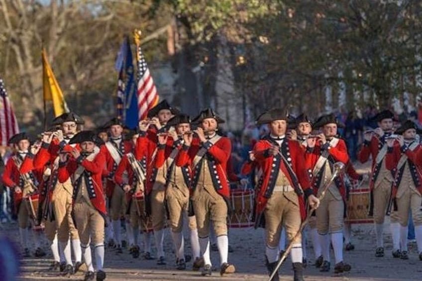 A group of people in historical military uniforms marching with flags. 2