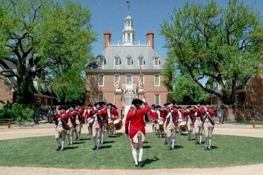 A group of people in historical uniforms marching in formation in front of a large brick building with a white steeple. 3