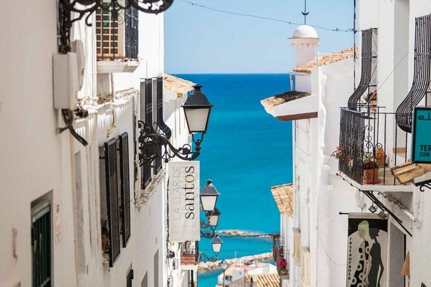 Une rue étroite bordée de bâtiments blancs, un lampadaire et une vue sur la mer. 4