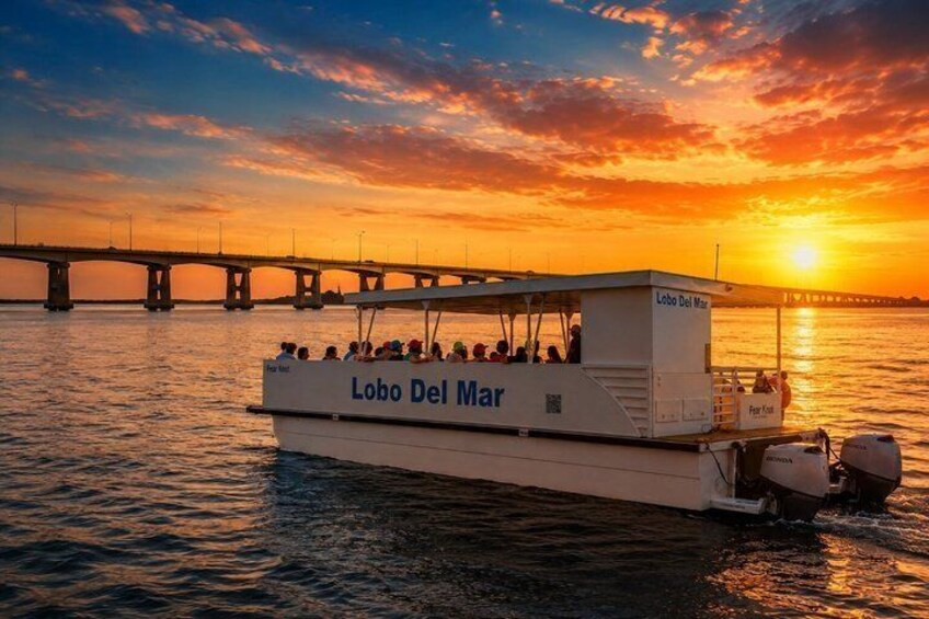 A boat named 'Lobo Del Mar' on the water with a sunset in the background and a bridge in the distance. 2