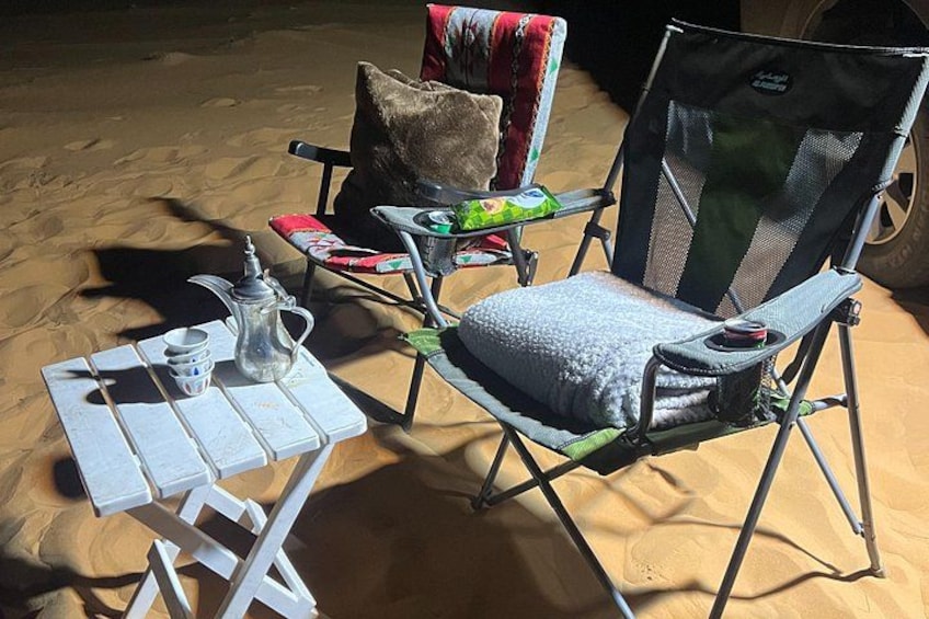 Un campamento con una mesa, sillas y una tetera sobre la arena. 3