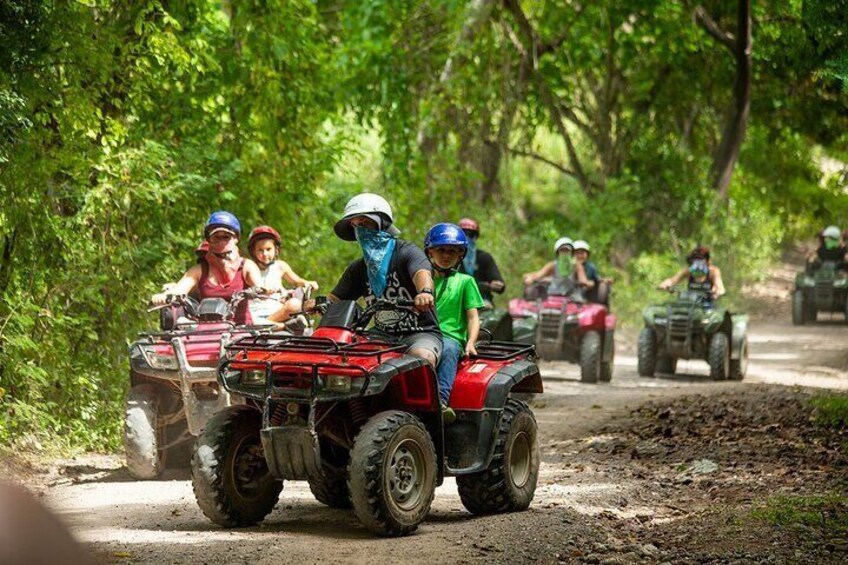 People riding ATVs on a dirt path surrounded by trees. 1